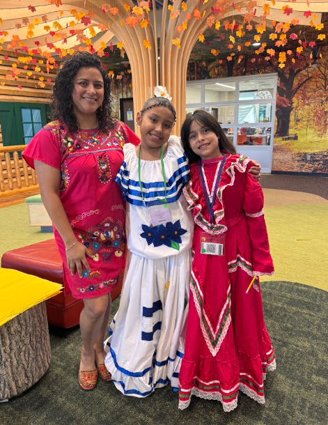 Ms. Fitch and two students in traditional clothing stand together, smiling.