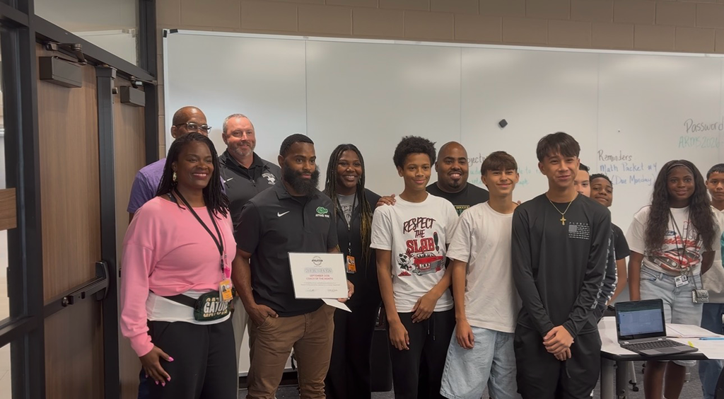 People standing in a room with a whiteboard behind them. Some hold certificates and others stand by a table.