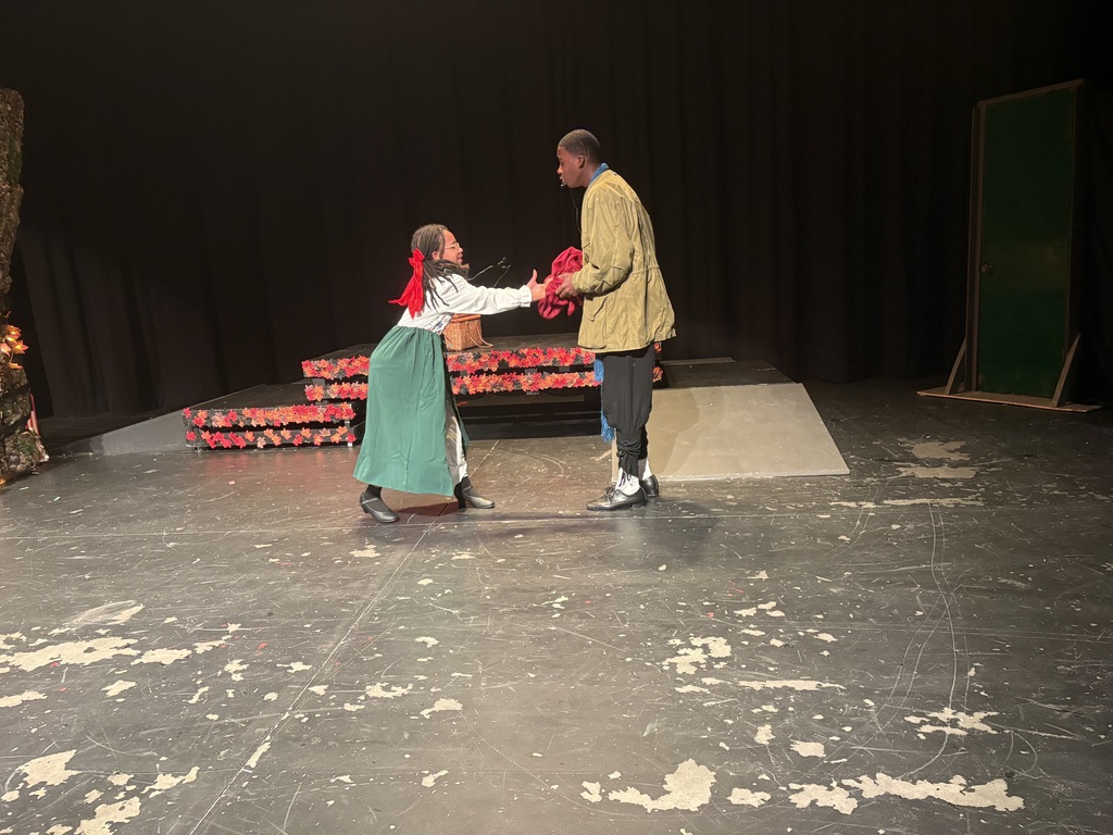 Two people on stage, one holding the other's hand, both looking at each other.