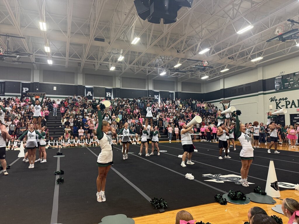 Cheerleaders performing in front of a cheering crowd at a school gym.