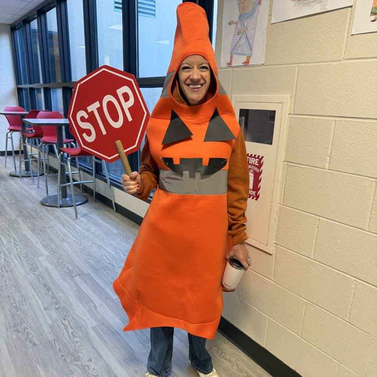 Person in orange costume holding a sign and standing in a hallway with white walls.
