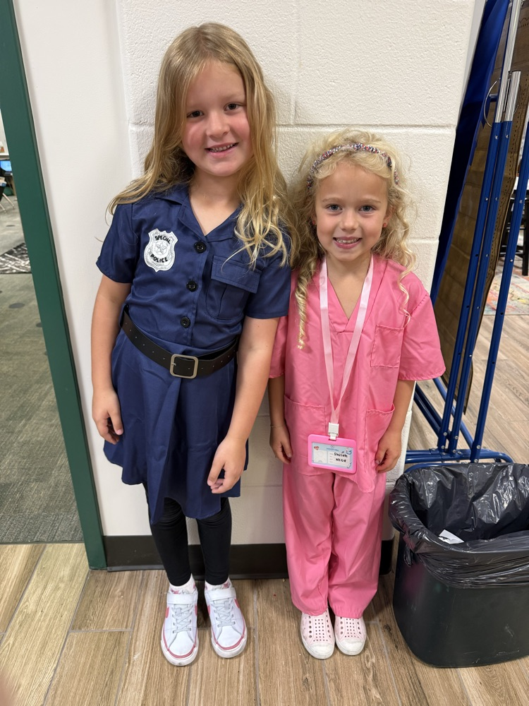 Two girls in uniforms, one in navy blue, the other in pink, stand near a trash can.