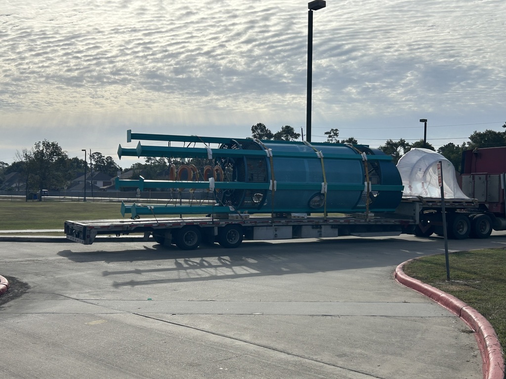 A large, green, cylindrical object on a truck with a tarp over it, parked on the road.