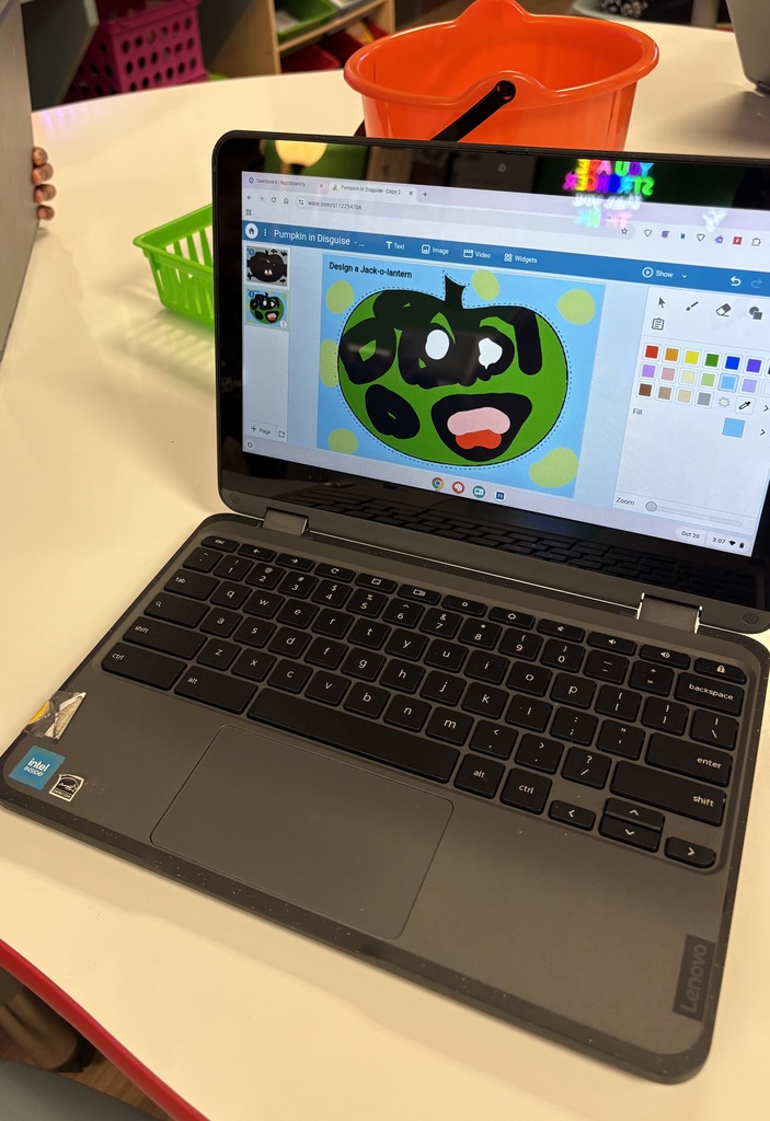 Laptop open to a cartoon face with a drawing app, a table with a green basket, and an orange bucket in background.