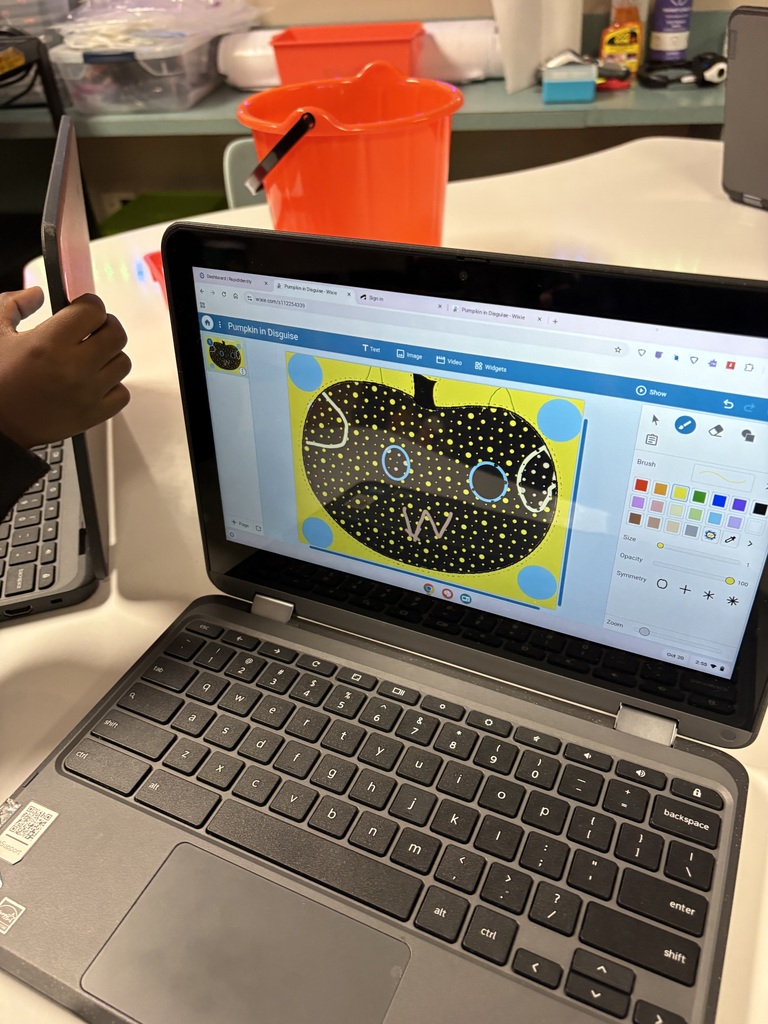 Laptop on a table, screen showing a drawing of a face, a bucket, and a pen.