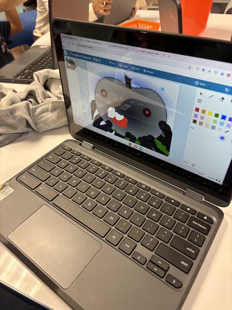 Open laptop with a drawing of a creature on the screen, with a keyboard, mouse pad, and clothing in background.