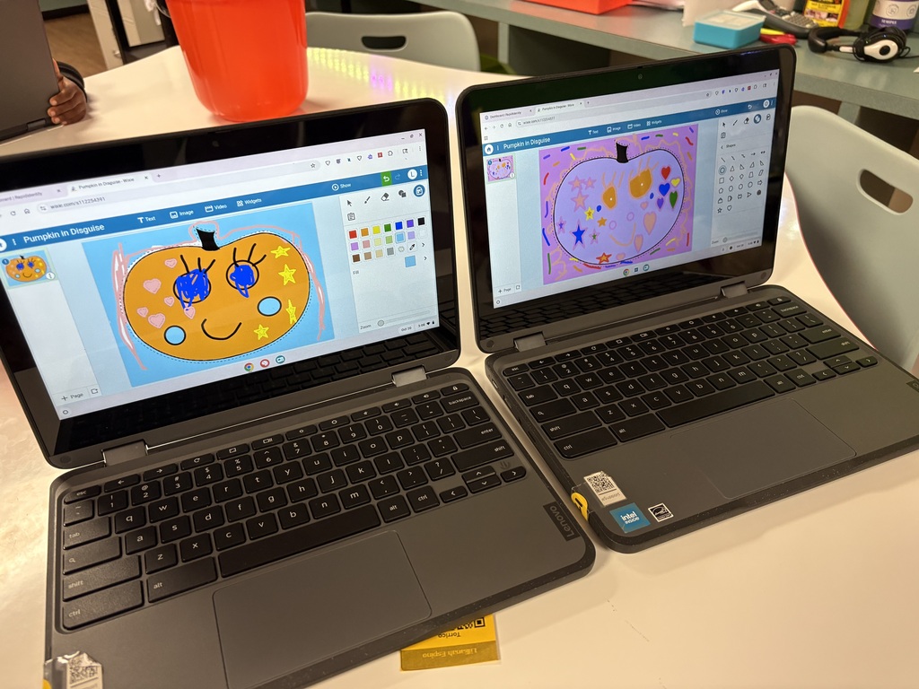 Two laptops with drawings displayed on screens on a white table with an orange bucket and chairs.