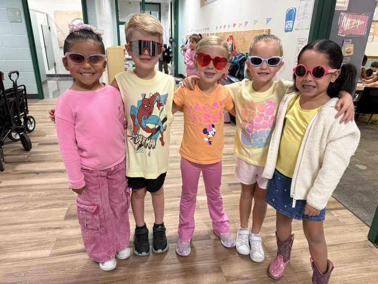 Five children wearing sunglasses stand in a hallway, smiling for the camera. A stroller is visible in the background.