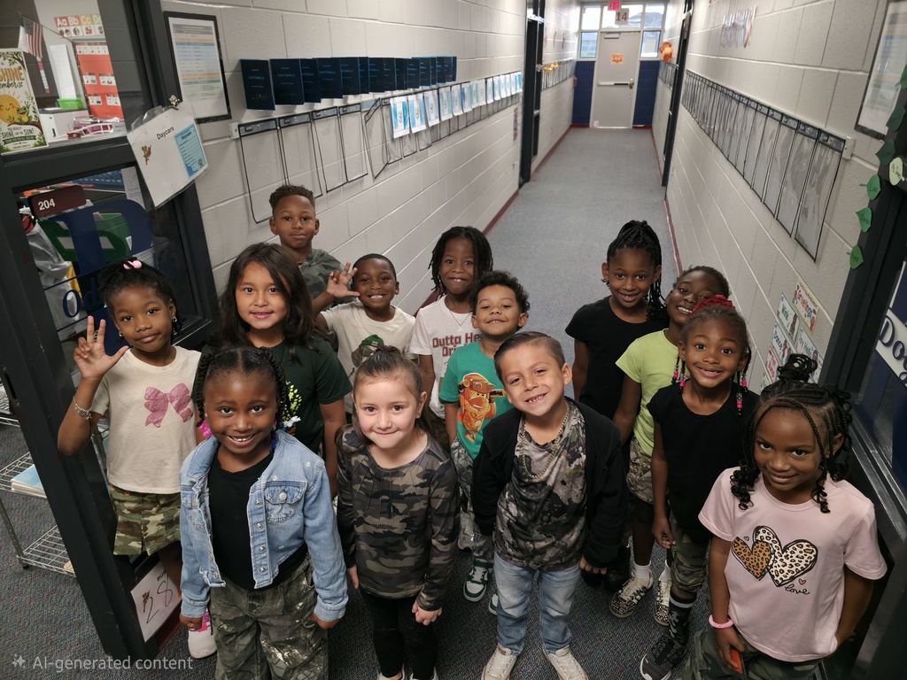 Group of children standing in a hallway, smiling, some waving; one holding a sign.