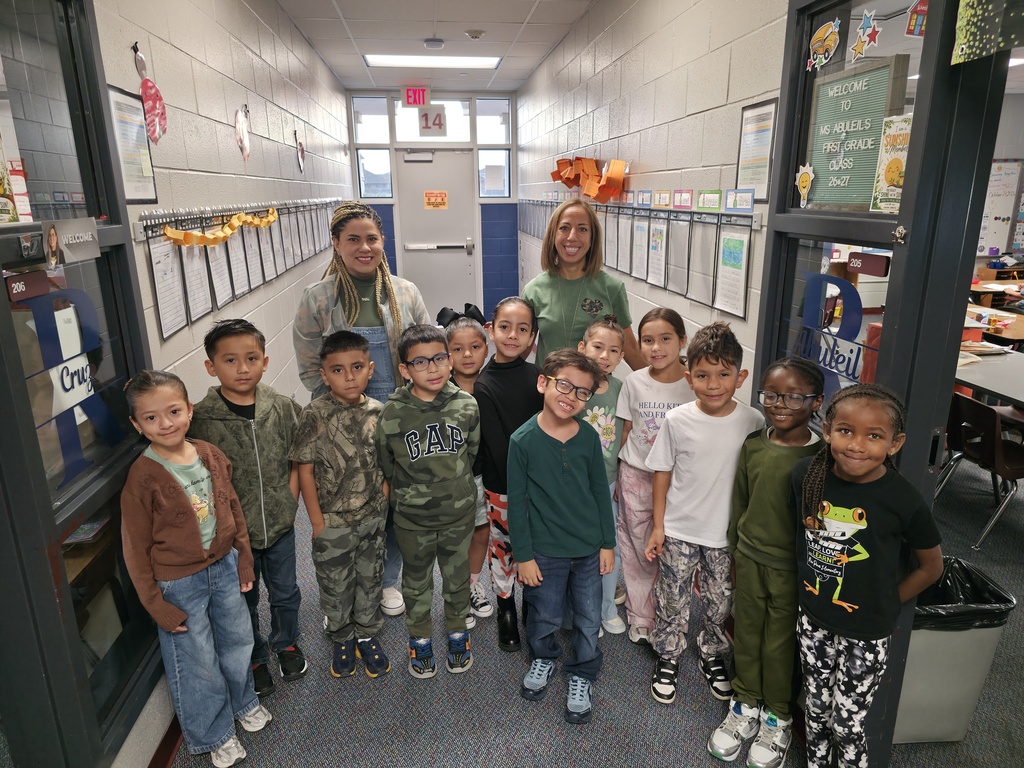 A group of children in uniform stands in a hallway. Two adults are standing behind them.
