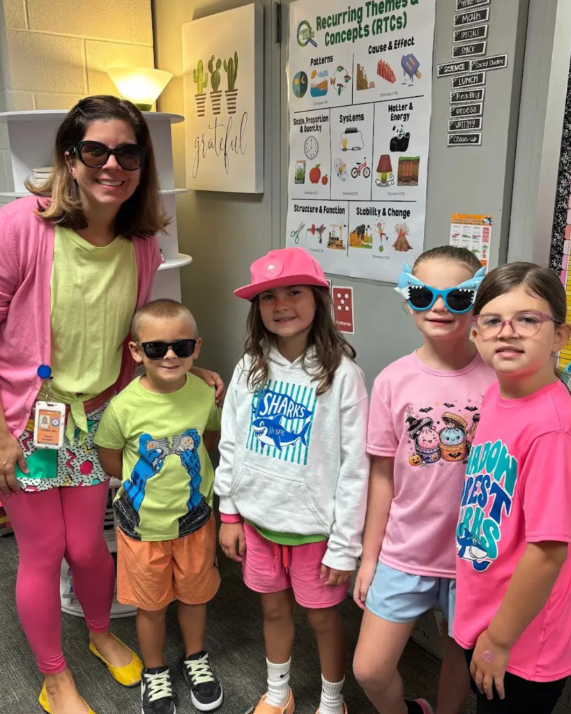 Adult woman with five children; all wearing sunglasses. Three girls in pink shirts, one girl in white, one boy in green.