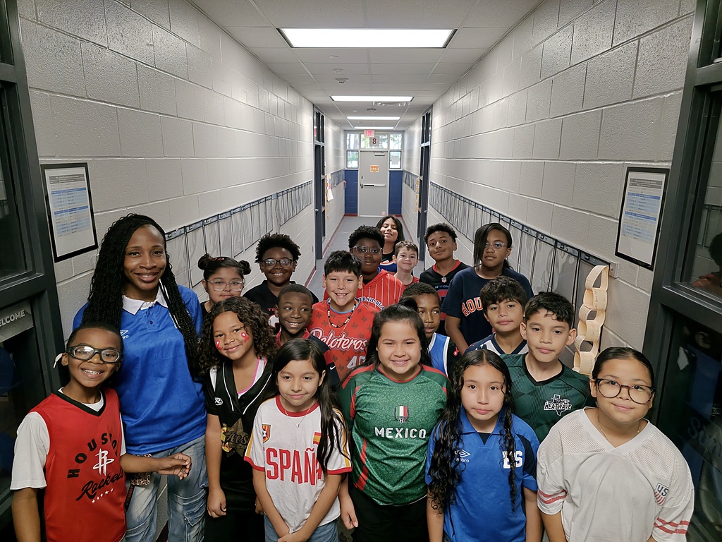 Group of students and an adult stand in a school hallway, smiling and looking at the camera.