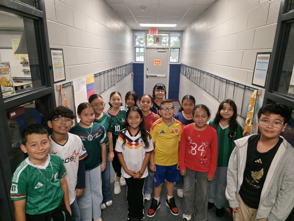 A group of children in sports jerseys pose for a picture in a brightly lit hallway.
