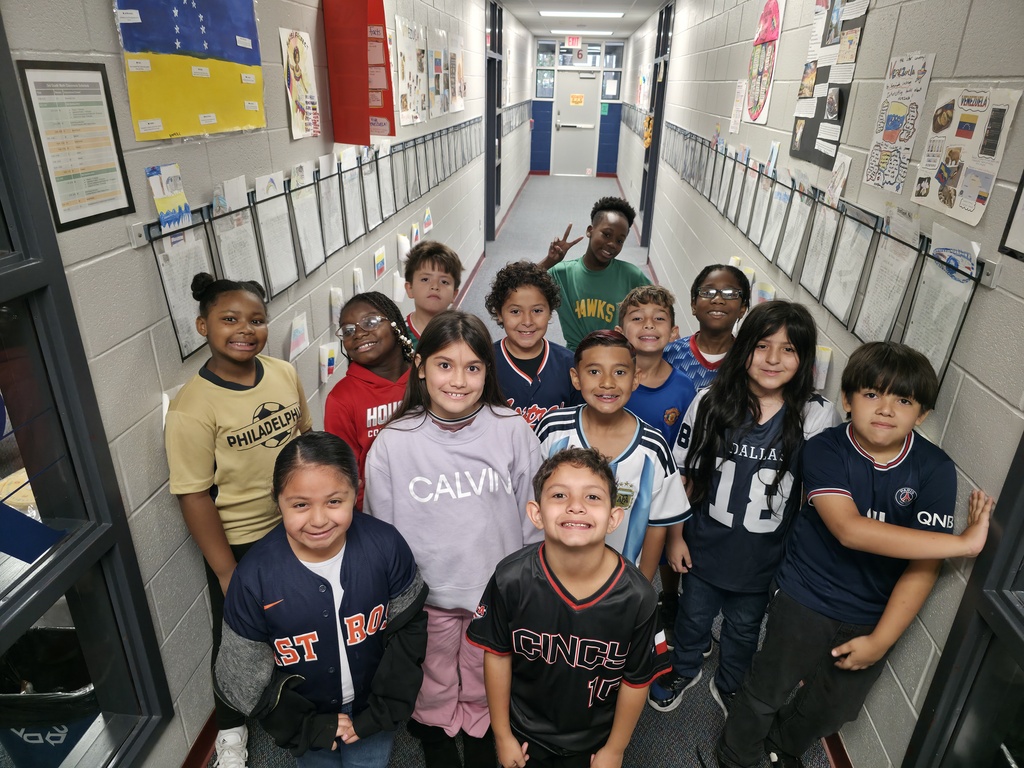 Group of children standing in a hallway with posters and bulletin boards on the walls.