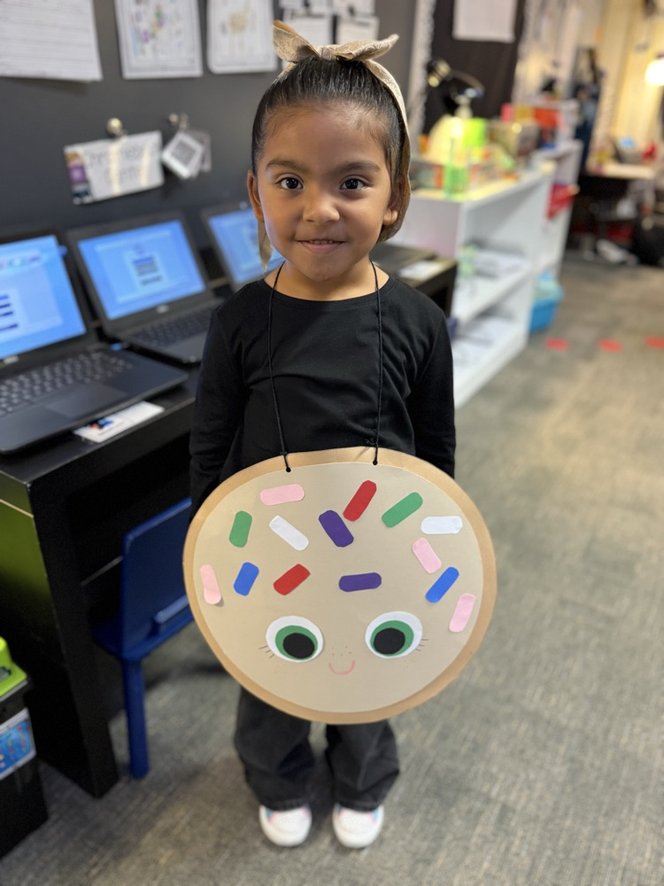 A young girl wearing a black shirt holds a round cardboard cutout of a donut with sprinkles.