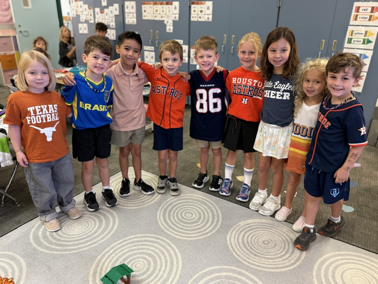 Several students stand in a line, smiling, in a classroom with a carpeted floor.
