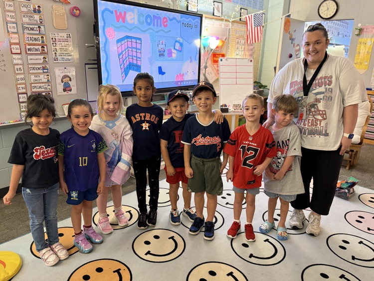 Several young children stand on a floor with smiley faces in front of a teacher.