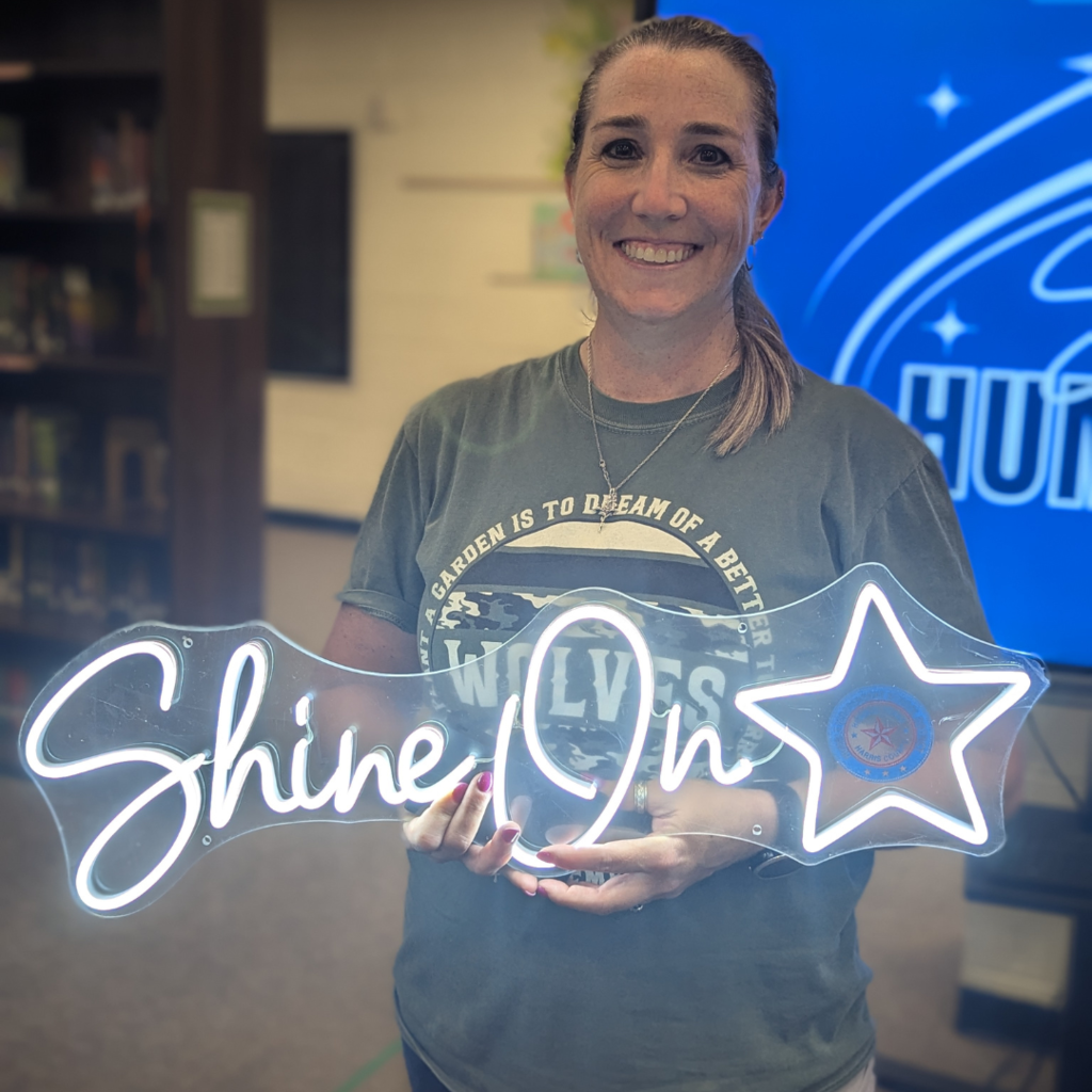 Mrs. Curry smiling while holding a neon "Shine On" award