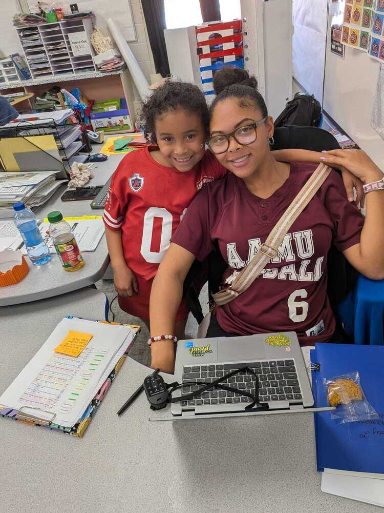 A teacher and student wearing college shirts smiling behind a desk