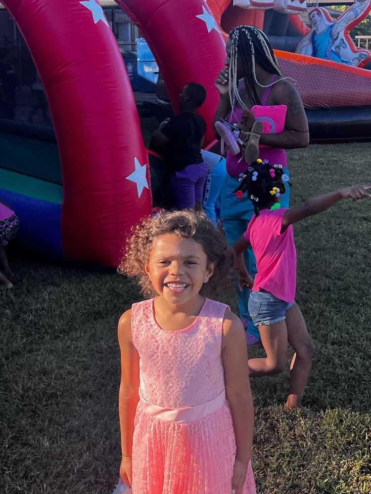 A young girl smiles in front of a colorful moon bounce while other children play in the background during the Fall Festival at Rolling Hills Elementary School.