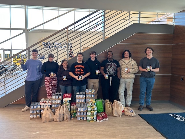 Students stand behind cases of cans for donation at the Center for Technology