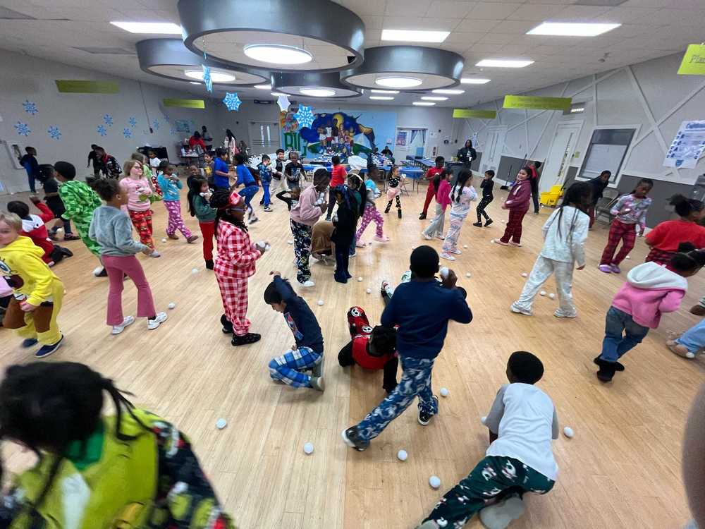 Students in pajamas enjoy an indoor PBIS Snow Day snowball fight, tossing soft “snowballs” and playing together in the school gym