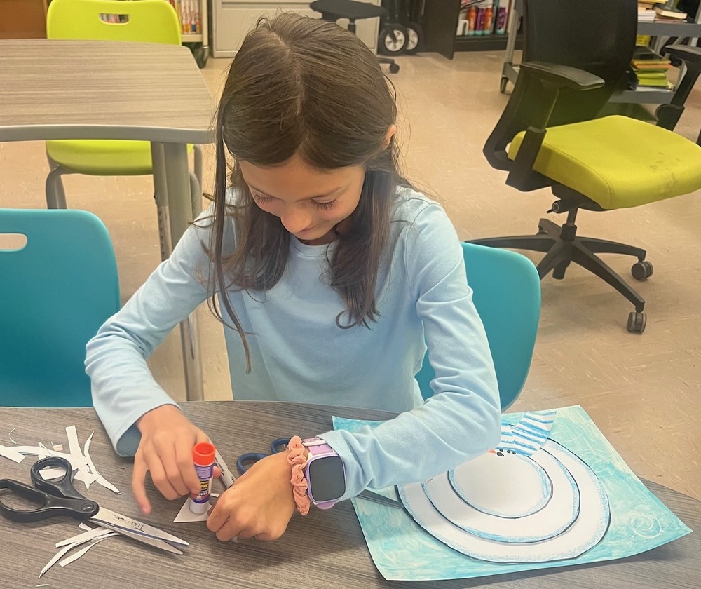 Fourth grader, Aurora Perry,  cuts construction paper to finish her snowman art project.
