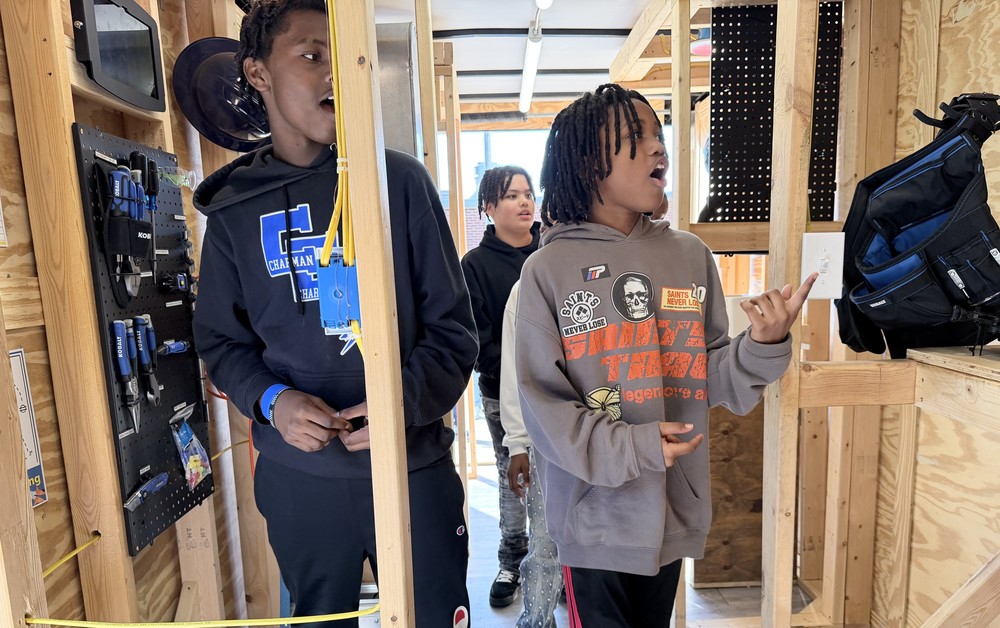 Two students explore the interior of a wooden portable classroom, observing the framing and electrical components.