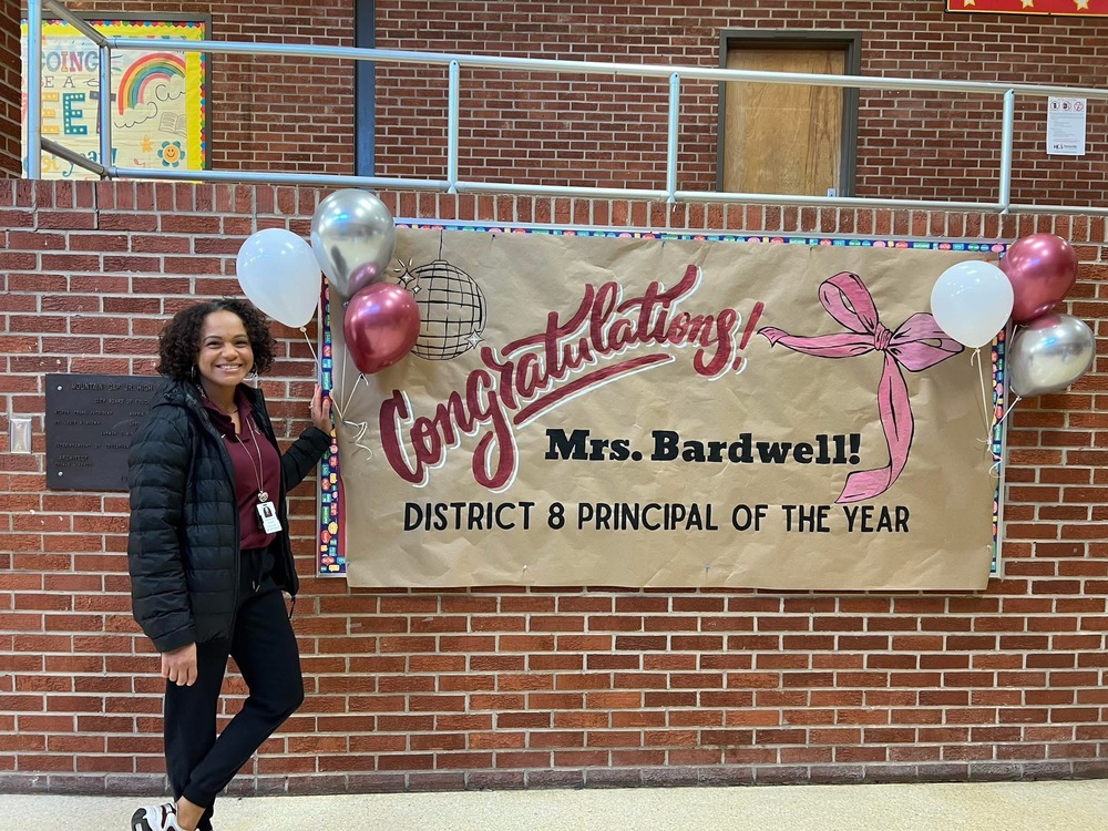 Mrs. Bardwell in front of a sign that says Congratulations on District 8 Principal of the Year