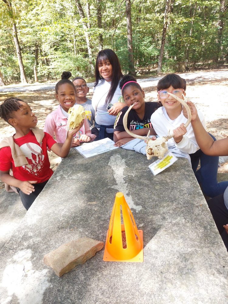 An adult and 5 third grade students outside on a picnic table with a collection of fossils.