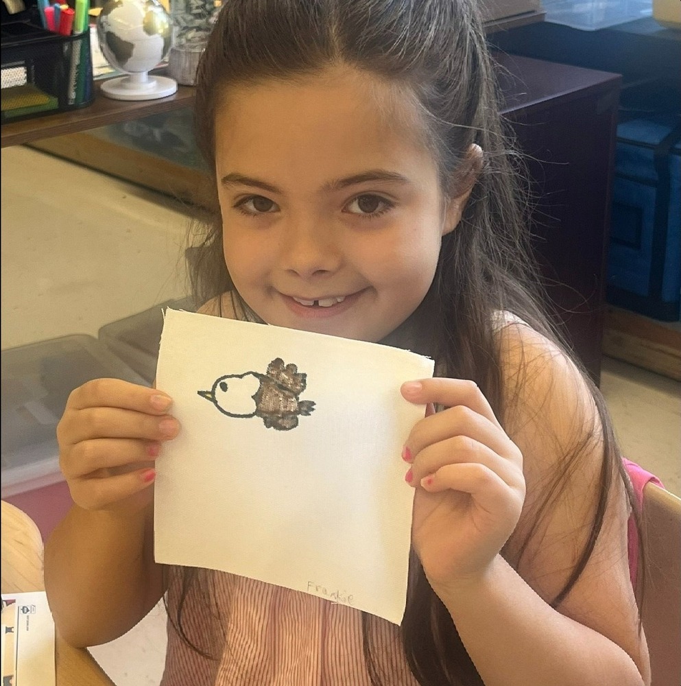 Fourth grade female students holds up her project tile with an eagle she drew on it.