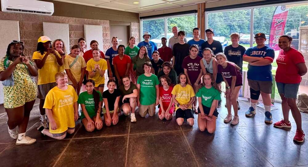 A group of students dressed in their house colors (yellow, green, red and blue). There are windows behind them.