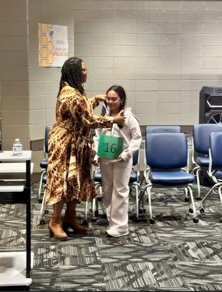 Teacher placing the 1st place medal on the little girl who won the Spelling Bee