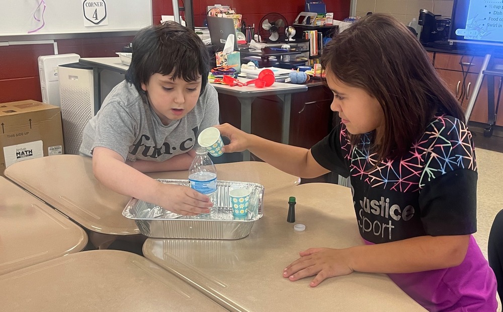 A male student and a female student work together mixing water and other ingredients to make elephant toothpaste.
