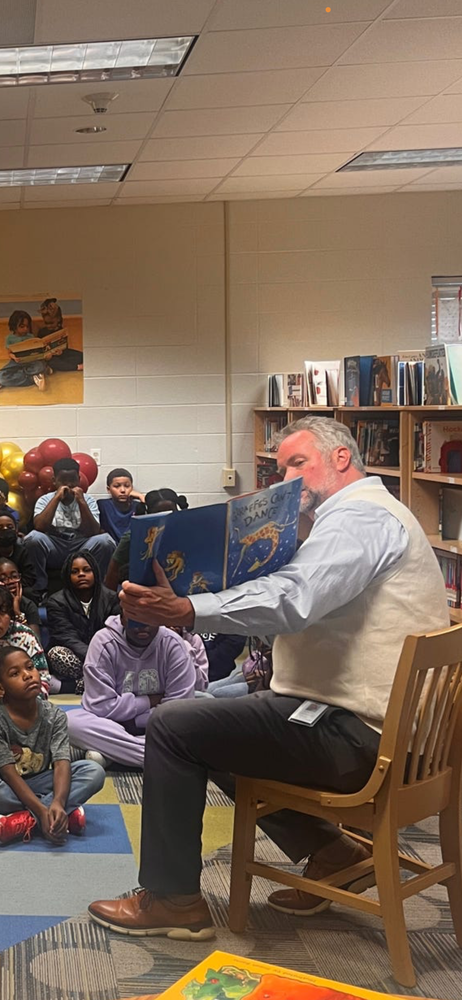 Deputy Superintendent A. J. Buckner reads a picture book to a group of students gathered in the school library.