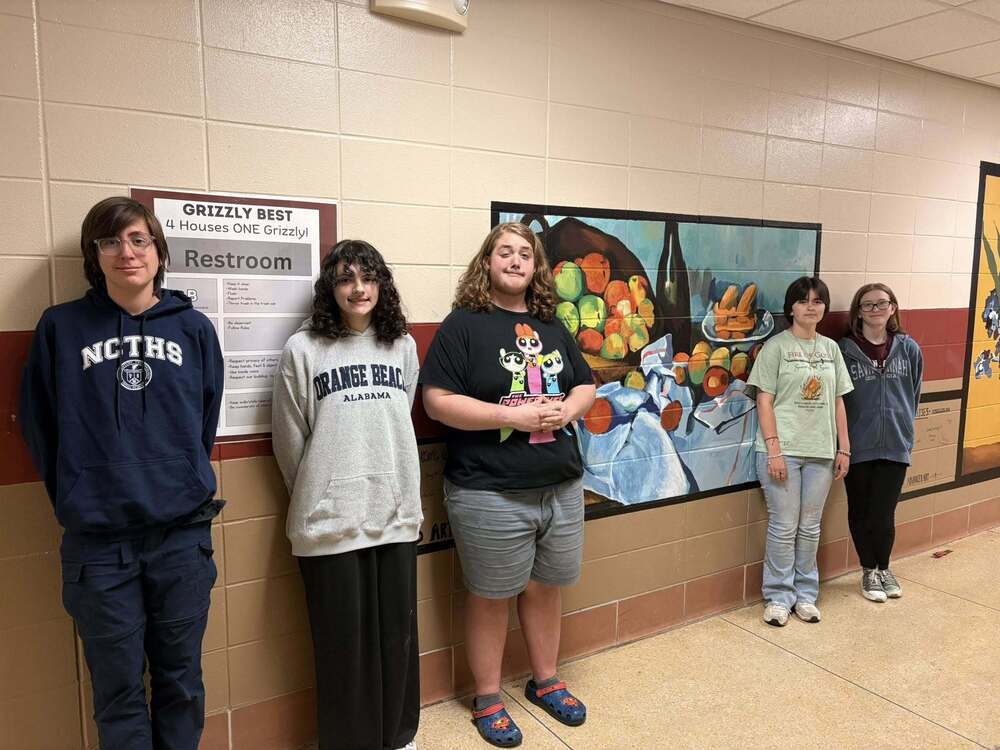 five 8th grade students who painted the mural standing in front of the mural they painted. The mural is a basked of fruit.