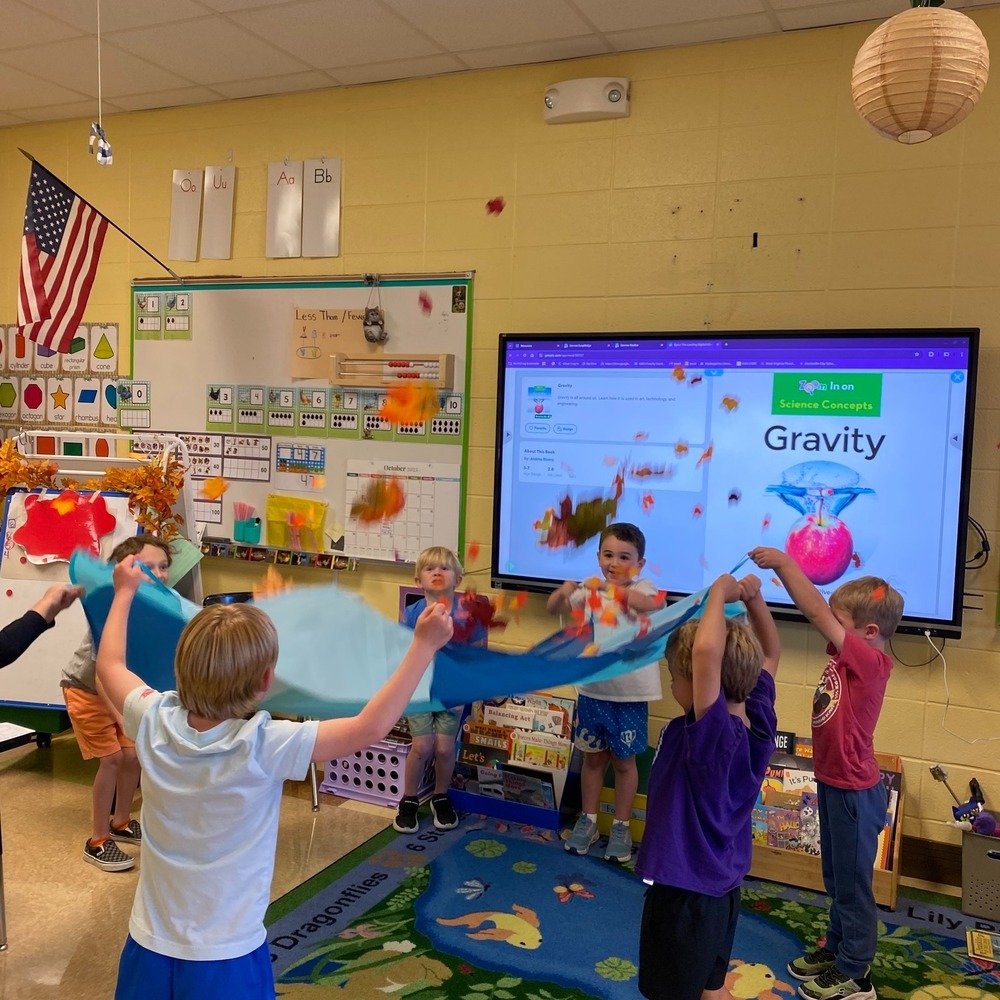 Kindergarten students use a parachute to bounce objects in the classroom.