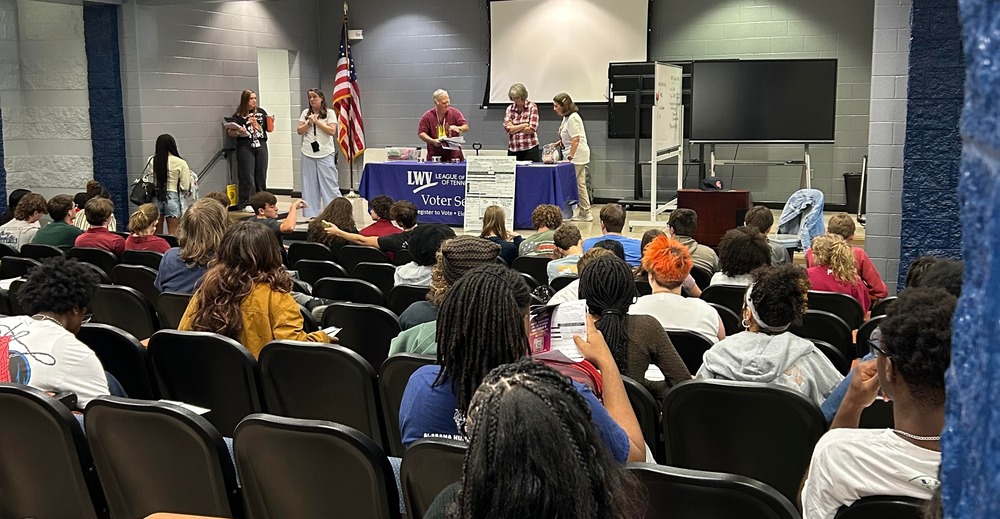 Students seated in auditorium listening to Principal white, who is introducing the League of Women Voters