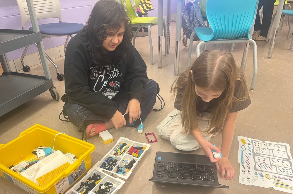 Two female students work together in a group to build a small robot. 