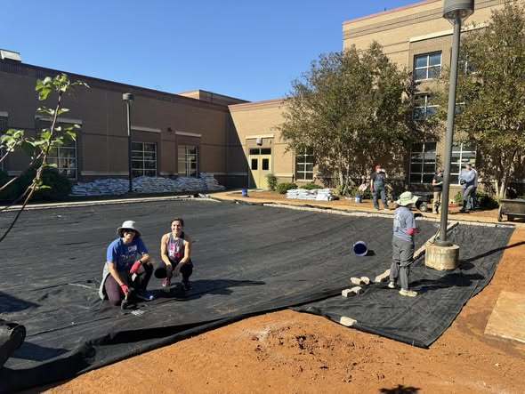 Volunteers work on laying down mesh in the Goldsmith Schiffman courtyard for the outdoor classroom