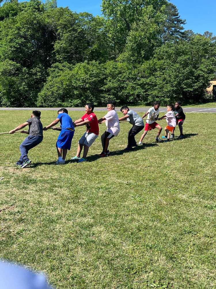 Elementary students playing tug-of-war during a sunny Field Day celebration outdoors.