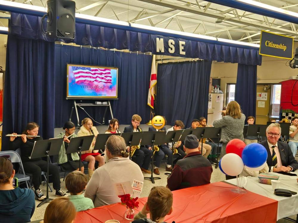 students sitting in row on stage playing musical instruments