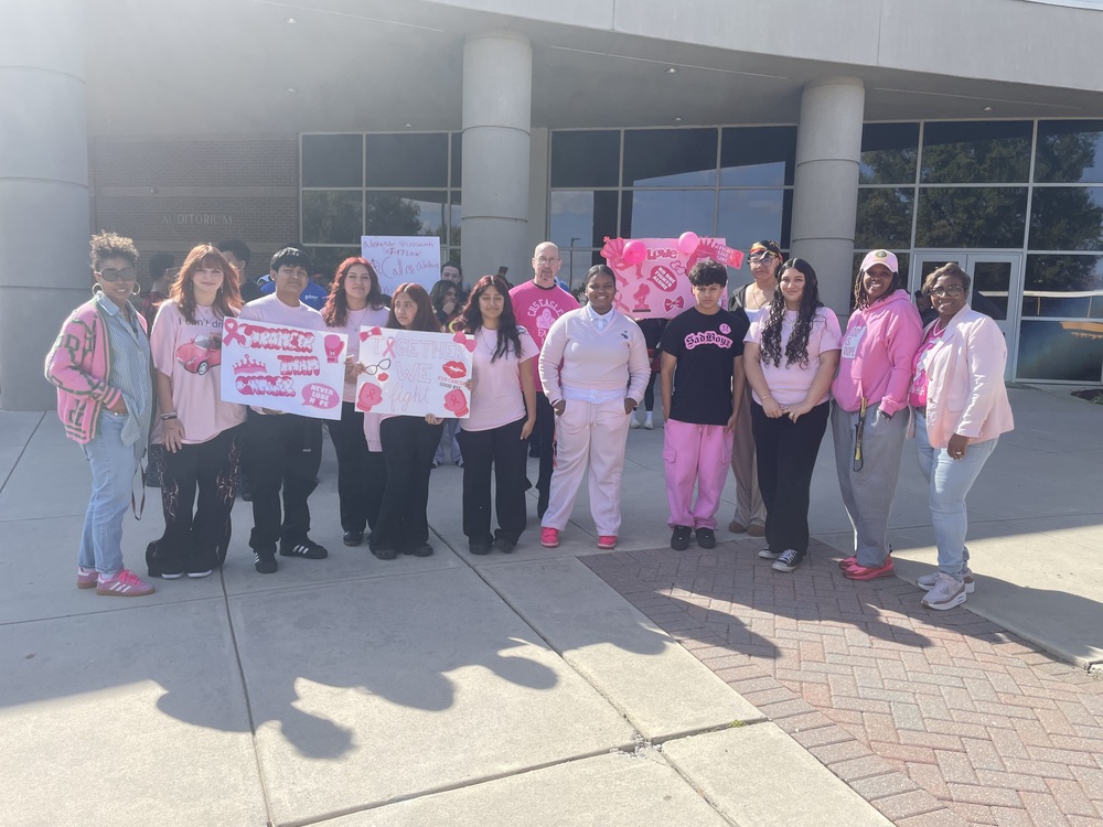 Future Business Leaders of America students standing in front of school wearing pink with teachers on each side wearing pink  while students are holding up breast cancer awareness poster inin pink and white
