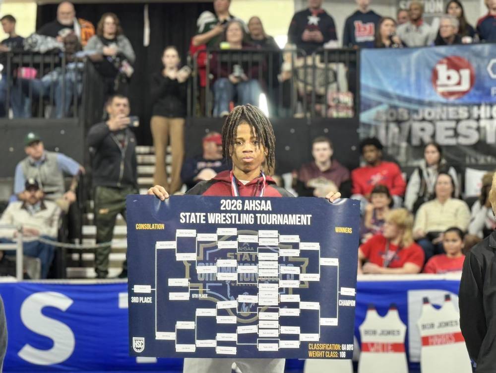 DeVaughn Miller pictured holding 2026 AHSSA State Wrestling Tournament Sign at state wrestling tournament after winning Class 6A 106 pound championship