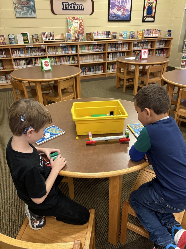 Two students at a round table using legos to build a hotel model in the library.