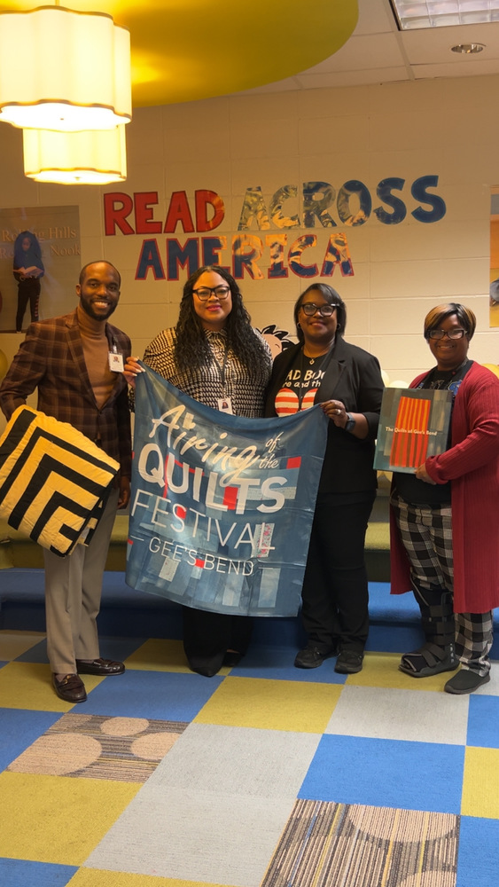 Larry Saulsberry, Principal Agun, and staff pose together during a Read Across America visit while displaying quilts and materials from Gee’s Bend.