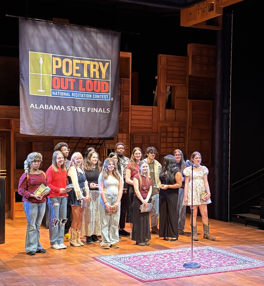 Lee High School Creative Writing Magnet students stand on stage holding awards at the Poetry Out Loud Alabama State Finals, with a “Poetry Out Loud” banner behind them.