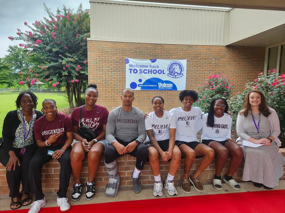 6 College students from Alabama A&M in school shirts are sitting outside the school with the school administrators sitting on each side of the group. They are in front of a sign that says "Welcome Back to School"