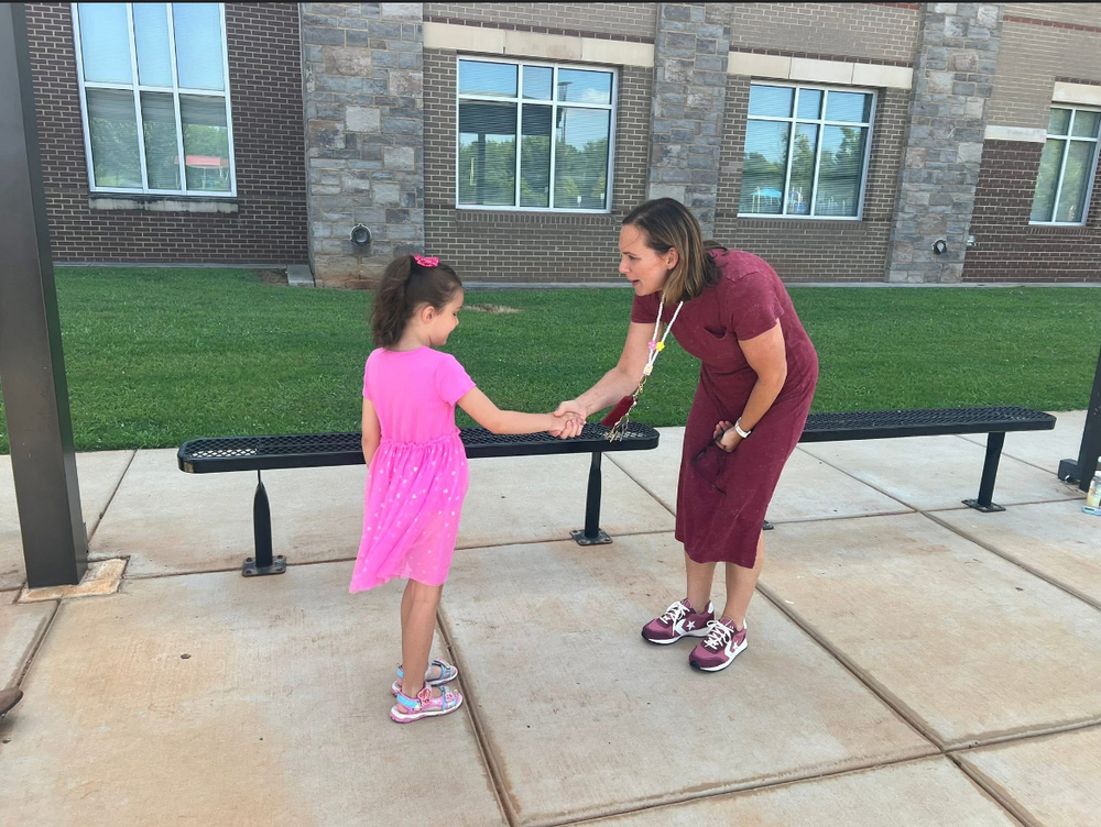 little girl and woman shaking hands in front of a school building