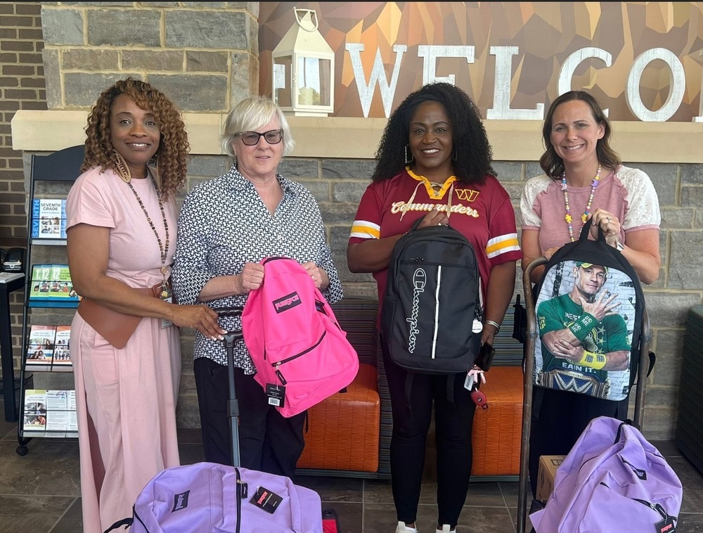 Four women standing in a school lobby holding backpacks